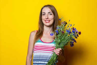 Sarı arka planda bir buket çiçekle çizgili elbiseli neşeli genç kadın.