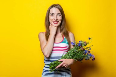 Sarı arka planda kır çiçekleri tutan çizgili elbiseli, güler yüzlü genç kız.