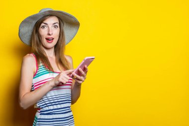 Beklenmedik bir şekilde elinde bir telefon, şapka ve çizgili elbiseyle sarı arka planda poz veriyor.