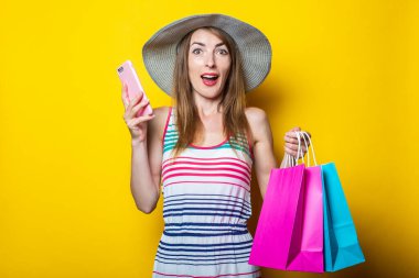Şapkalı genç bir kadının elinde telefon ve sarı arka planda alışveriş torbaları olmasına şaşırdım.