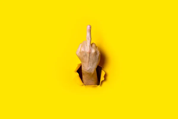 Man's hand showing middle finger, fuck on a yellow background. Hand gestures.