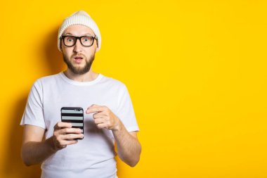 Sakallı, şaşırmış genç adam sarı arka plandaki telefonu işaret ediyor..