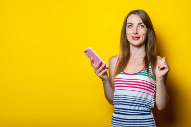 Sarı arka planda elinde telefon tutan cana yakın, sevimli genç bir kadın..