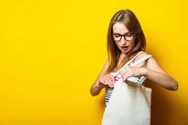 Sarı arka planda alışveriş yapan keten çantaya bakan genç bir kadın.