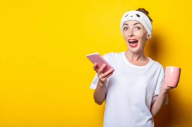 Bandajlı, sarı arka planda bir fincan kahvesi olan neşeli, şaşkın bir genç kız..