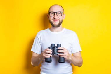 Sarı arka planda dürbün tutan sakallı, gülümseyen genç adam..