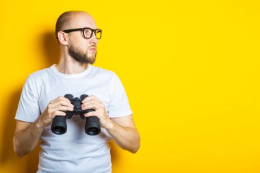 Sarı arka planda dürbünü tutan sakallı, ciddi bir genç adam..
