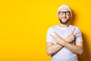 Şapkalı ve gözlüklü genç adam elleri ve kolları çapraz ve iki parmağı havada hareketler gösteriyor.