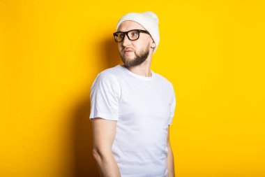 Sarı arka planda şapkalı, gözlüklü, sakallı yakışıklı bir genç.