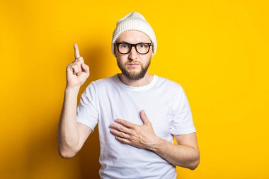 Ciddi sakallı genç adam elini sarı arka planda göğsüne koydu.