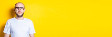 Sarı arka planda beyaz gömlekli, sakallı, güzel kel bir adam. Pankart