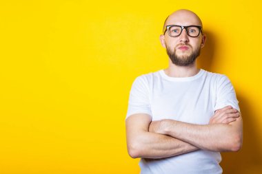 Sarı arka planda beyaz tişörtlü, gözlüklü, sakallı, ciddi, kel bir genç.
