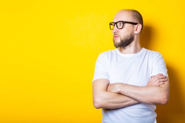 Ciddi sakallı genç adam sarı arka plana bakıyor.