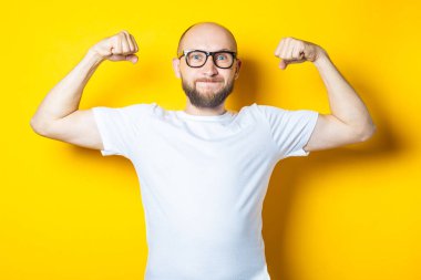 Sakallı yakışıklı, güçlü genç adam sarı arka planda kaslar gösteriyor.