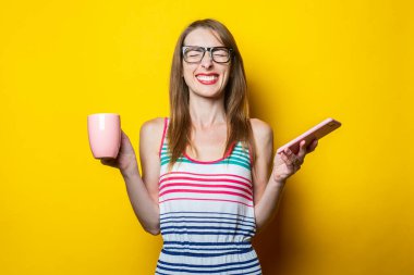 Genç bir kadın, gözlüklü, gözlüklü, telefonlu ve elinde kahve fincanı olan sarı bir kadın..