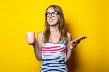 Gülümseyen genç bir kadın. Sarı arka planda telefonla kahve içiyor..