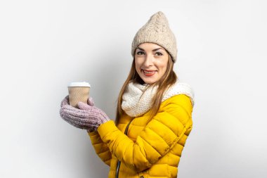 Sarı ceketli ve şapkalı genç bir kadın arka planda bir bardak kahve ya da çay tutuyor. Duygusal kahkaha, sürpriz, öpücük. Konsept kış, sonbahar, kahve evi.
