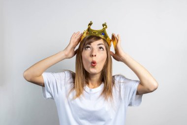 Kafasında taç olan genç bir kadın ve hafif bir arka planda şaşırmış bir yüz. Duygusal kahkaha, sürpriz, öpücük, şok. Kraliçe konsepti, şans, en iyisi, kazanmak, zafer. Pankart.