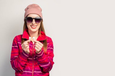 Gözlüklü, şapkalı, pembe ceketli, gülen yüzlü, kablosuz kulaklıklı arkadaş canlısı genç bir kadın. Modern tarz kavramı, havalı müzik. Yüz ifadesi. Pankart.