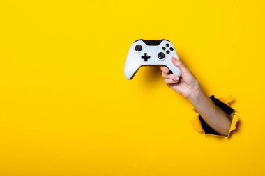 Kadın eli, parlak sarı bir arka planda joystick tutuyor..