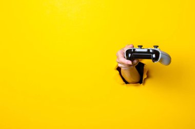 Kadın eli, parlak sarı bir arka planda joystick tutuyor..