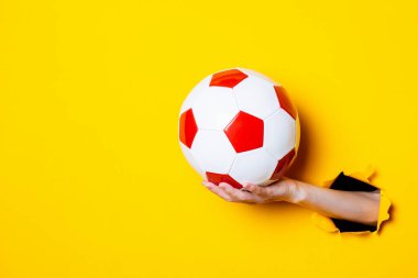 Kırmızı beyaz, parlak sarı arka planda futbol topu tutan bir kadın..