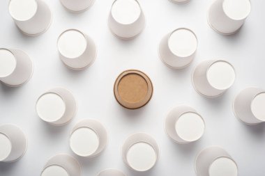 Açık arkaplanda bir sürü beyaz ve bir tane kahverengi kağıt bardak var. Üst manzara, düz uzanma