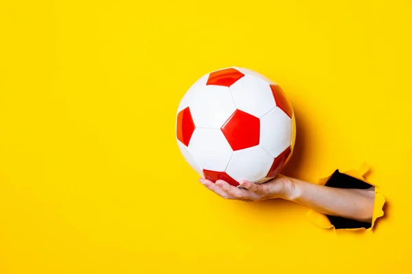 女子手拿着一个红白相间的足球 背景是明亮的黄色 — 图库照片