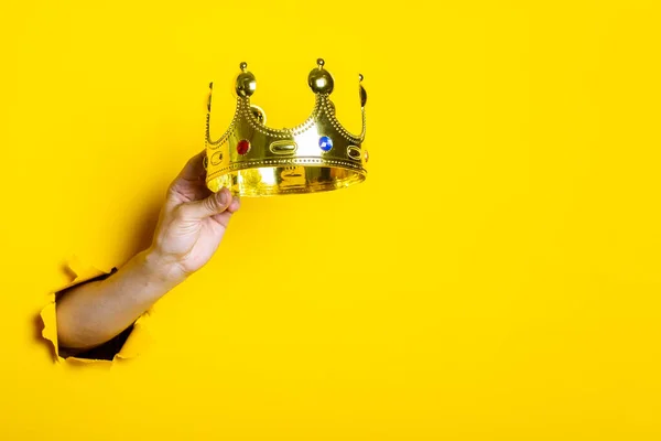 Female hand holds a gold crown on a bright yellow background