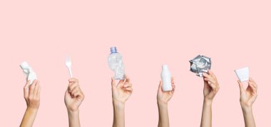 Eller çöpü açık pembe arka planda tutuyor. Ayrı çöp kavramı, plastiği durdur, geri dönüşümü durdur.