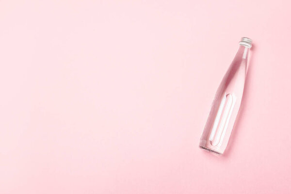 Стеклянная бутылка с чистой водой на розовом фоне. Концепция здравоохранения, водного баланса, красоты и здоровья. Баннер. Плоский, вид сверху.