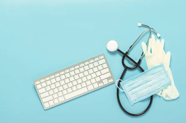 Keyboard, medical stethoscope, latex gloves and a protective mask on a blue background. Concept medicine, hospital, safety, epidemic, doctor\'s call, online, consultation. Banner. Flat lay, top view.