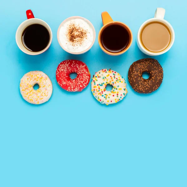 Tasty donuts and cups with hot drinks, coffee, cappuccino, tea on a blue background. Concept of sweets, bakery, pastries, coffee shop, meeting, friends, friendly team. The square. Flat lay, top view.