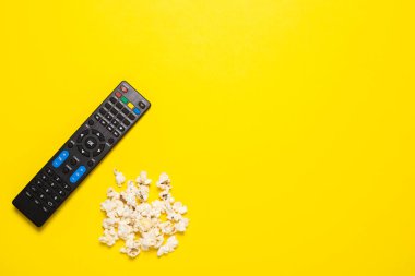 TV uzaktan kumandası, TV ayarlayıcısı ya da ses sistemi ve sarı arka planda patlamış mısır. Kavram serisi, film, spor. Pankart. Düz yatış, üst görünüm.