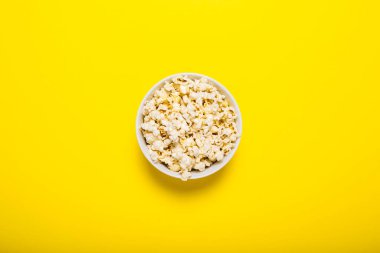 Sarı arka planda patlamış mısır kasesi. Kavram serisi, film, spor. Pankart. Düz yatış, üst görünüm.