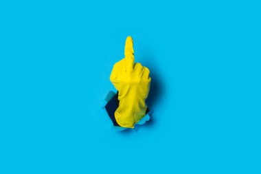 Hand in yellow glove showing middle finger on a bright blue background. clipart
