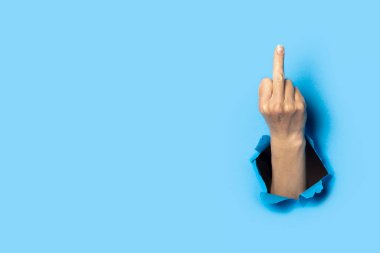 Hand shows the gesture of the middle finger on a blue background. Offensive gesture, fuck off, leave me alone.