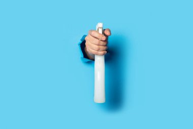 Adamın eli parlak mavi arka planda bir sprey tutuyor..