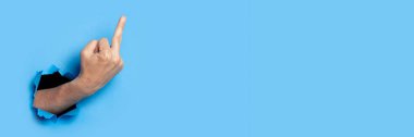 Hand shows the gesture of the middle finger on a blue background. Offensive gesture, fuck off, leave me alone.