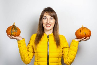 Sarı ceketli güzel genç kız arka planda iki balkabağı tutuyor. Cadılar Bayramı konsepti, sonbahar, kutlama. 