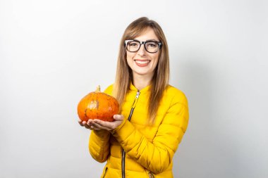 Sarı ceketli güzel genç kız arka planda bir balkabağı tutuyor. Cadılar Bayramı konsepti, kutlama.