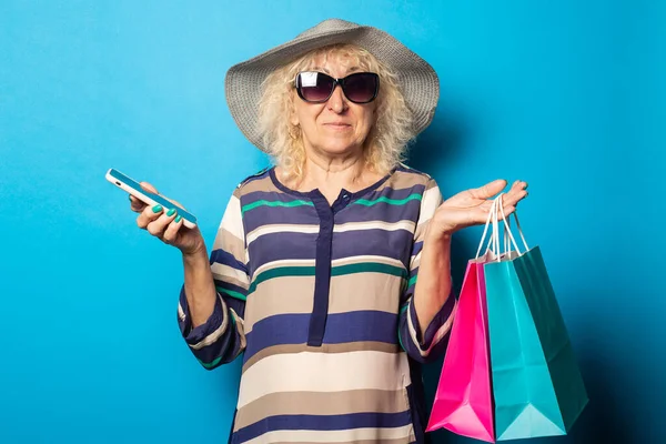 Mulher Velha Com Óculos Detém Sacos Compras Telefone Fundo Azul — Fotografia de Stock