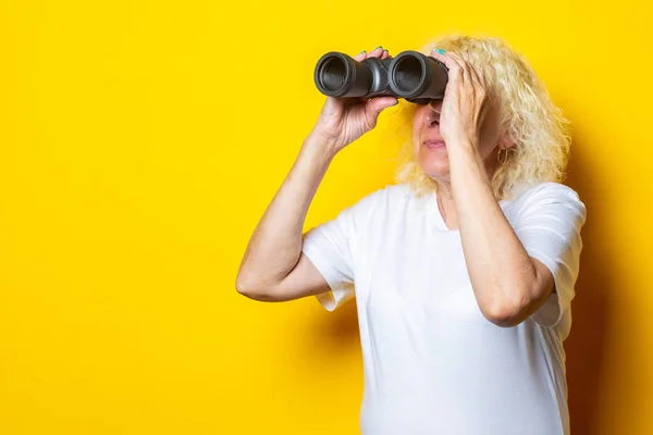 Beyaz Tişörtlü Yaşlı Kadın Sarı Arka Plandaki Dürbünle Bakıyor — Stok fotoğraf
