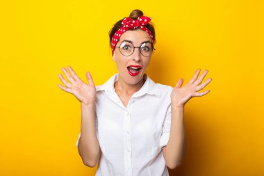 Şaşırmış yüzlü, gözlüklü ve sarı arka planda saç bandı takan genç bir kadın..