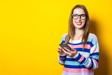 Gülümseyen genç bir kadın sarı arka planda bir telefon tutuyor. Pankart.