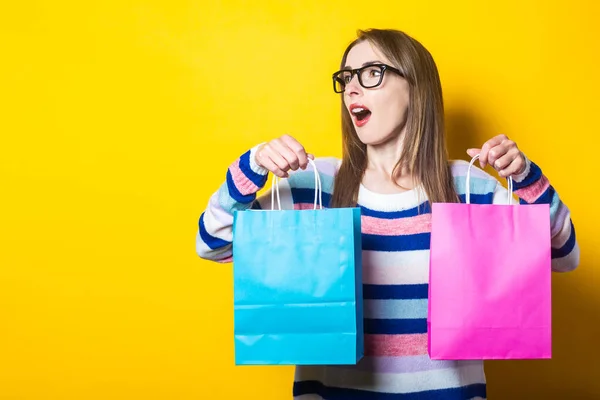 セーターの若い女性は黄色の背景に購入とショッピングバッグを保持しています — ストック写真