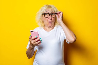 Sarı arka planda telefonu tutan yaşlı kadına şaşırdım.