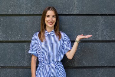 Dost canlısı genç bir kadın, taş duvar arkasında jest yapıyor..