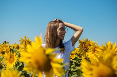 Güneşli bir yaz gününde, beyaz tişörtlü ve gözlüklü genç bir kadın..