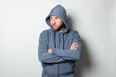 Ciddi, agresif bir yüzü olan kapüşonlu genç bir adam hafif bir arka planda yana bakıyor..